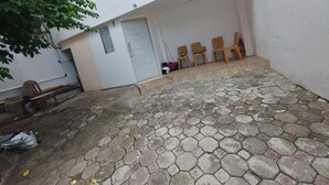 Ein Innenhof mit einem weißen Gebäude, einem gepflasterten Bereich aus Stein und Holzstühlen.
