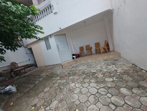 A courtyard with a white building, a stone-paved area, and wooden chairs. - Eiffel Residence Cideng by Zuzu (Jakarta)