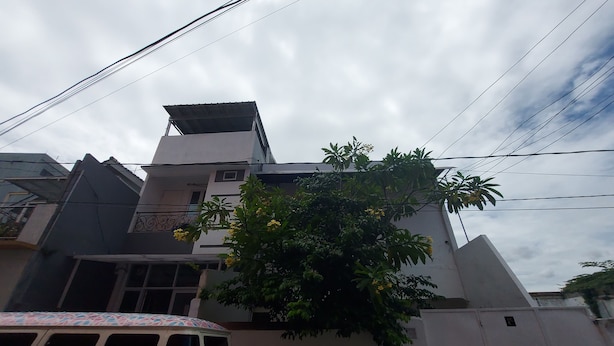 A building with a white facade, a balcony, and a tree with yellow flowers. - Eiffel Residence Cideng by Zuzu (Jakarta)