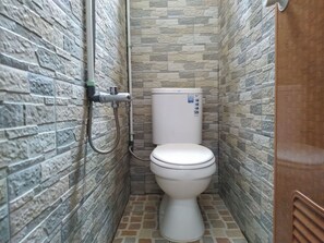 A small, stone-textured bathroom with a toilet and a shower head. - Eiffel Residence Cideng by Zuzu (Jakarta)