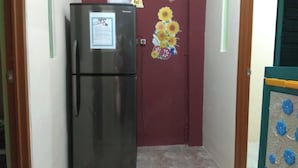 A hallway with a refrigerator, a maroon door, and a wall with a sunflower decoration. - Eiffel Residence Cideng by Zuzu (Jakarta)