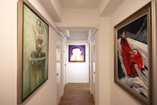 A hallway with framed artworks on the walls, a wooden floor, and white doors. - Apple Hotel (Hong Kong Island)
