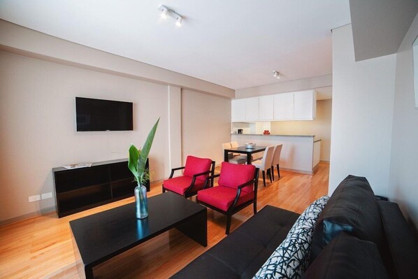 A modern living room with a black sofa, red chairs, a black coffee table, and a TV mounted on the wall. - ARC Callao Studios & Suites (Buenos Aires)