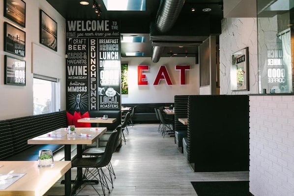 A modern restaurant interior with a central 'EAT' sign, tables, chairs, and a wall with various food-related words. - Hotel Solarena Bw Premier Collection Newport Beach (Newport Beach)