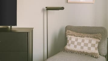 Une pièce avec un bureau de couleur foncée, une chaise de couleur claire dotée d’un coussin à carreaux, un grand lampadaire et un tableau encadré accroché au mur.