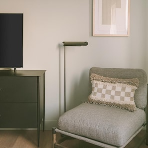 A room with a dark-colored desk, a light-colored chair with a checkered cushion, a tall floor lamp, and a framed picture on the wall. - Hotel Solarena Newport Beach, a Dazzler Select by Wyndham (Newport Beach)