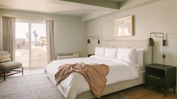 Une chambre à coucher avec un lit, une chaise, une table de chevet, une lampe et une fenêtre avec des rideaux.