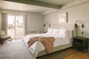 Un dormitorio con cama, una silla, una mesita de noche, una lámpara y una ventana con cortinas.