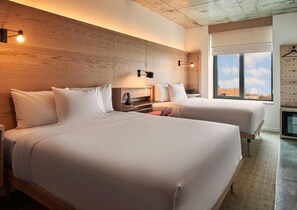 A hotel room with two beds, a wooden headboard, a nightstand, a small table, and a large window with a city view. - Radio Hotel (New York)