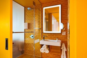 A bathroom with a glass shower enclosure, a white sink, and a mirror above it. - Radio Hotel (New York)