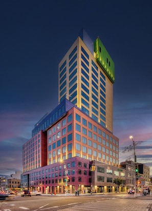 A multi-story hotel with a prominent green sign on top, a large number of windows, and a street view with traffic lights and pedestrians. - Radio Hotel (New York)