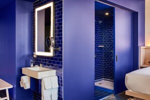 A modern bathroom with a blue-tiled shower, a sink with a mirror, and a bed in the adjacent room. - Radio Hotel (New York)