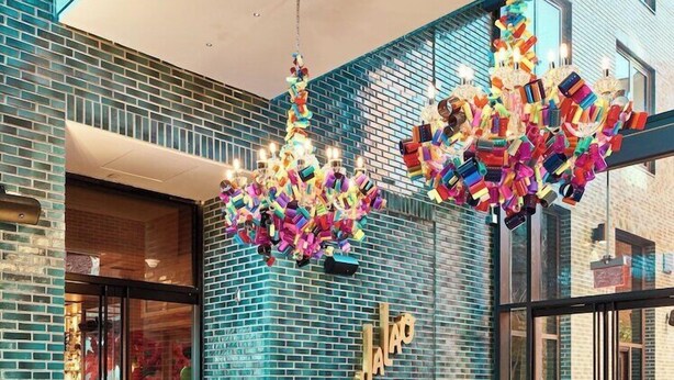 Un interior moderno con una pared de ladrillo, una lámpara de araña hecha con objetos de colores y dos sillones estampados.