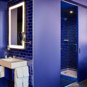 A bathroom with a large mirror, a sink, and a shower with blue-tiled walls. - Radio Hotel (New York)