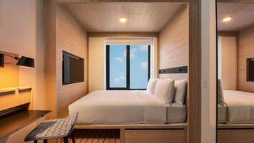 A compact hotel room with a bed, bedside table, chair, and a large window.