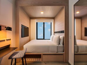 A compact hotel room with a bed, a desk, and a chair. There is a window with a view of the sky. - Radio Hotel (New York)