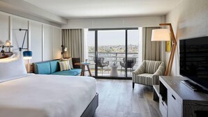 A hotel room with a bed, a sofa, a TV, a desk, and a balcony with a view. - Westdrift Manhattan Beach, Autograph Collection (Manhattan Beach)