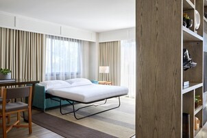 Una habitación de hotel con una cama, un escritorio, una silla, una lámpara y una estantería.