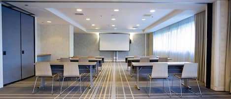 A conference room with a large screen, multiple tables, and chairs, carpeted floor, and a patterned wall.