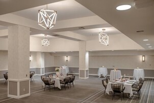 A spacious hotel dining area with tables set for meals, geometric ceiling lights, and a neutral color scheme.