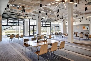 A modern conference room with large tables, chairs, and a large window with a view of greenery. - Westdrift Manhattan Beach, Autograph Collection (Manhattan Beach)