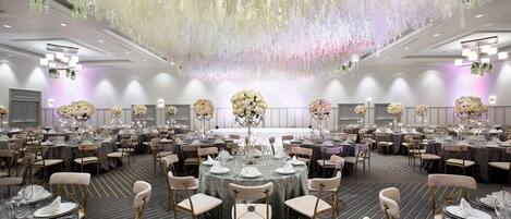 A large banquet hall with round tables, chairs, and hanging floral decorations.