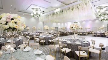 A banquet hall with round tables, chairs, and floral centerpieces.