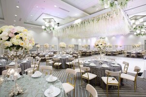 Un salón de banquetes con mesas redondas, sillas y centros de mesa florales.