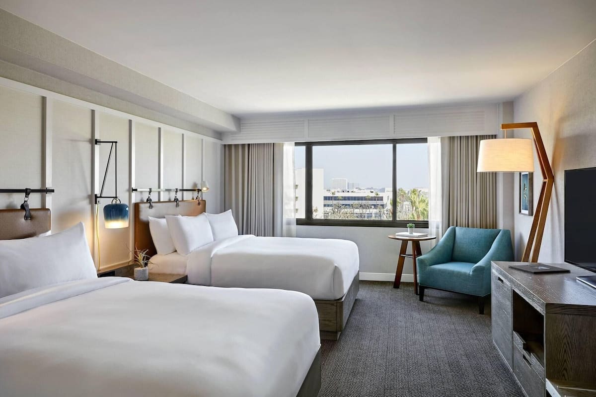 A hotel room with two beds, a TV, a desk, a chair, and a view of the city.