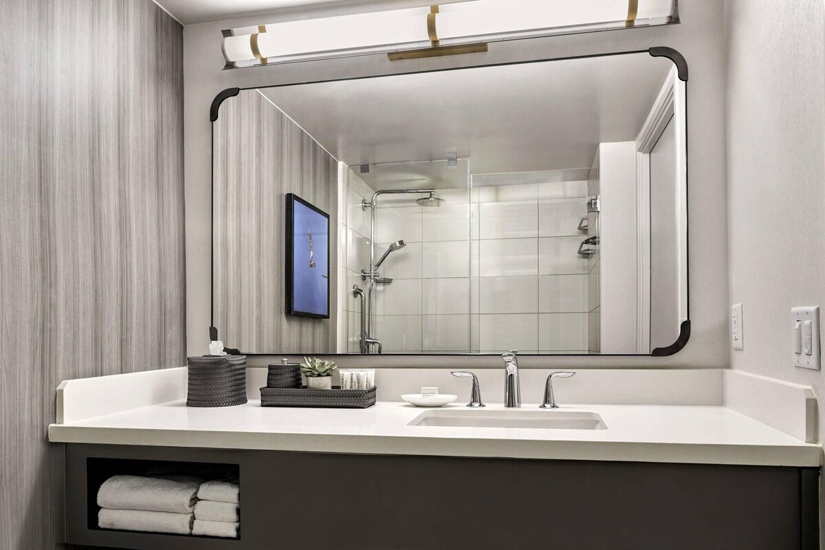 A modern bathroom with a large mirror, a sink, and a shower.