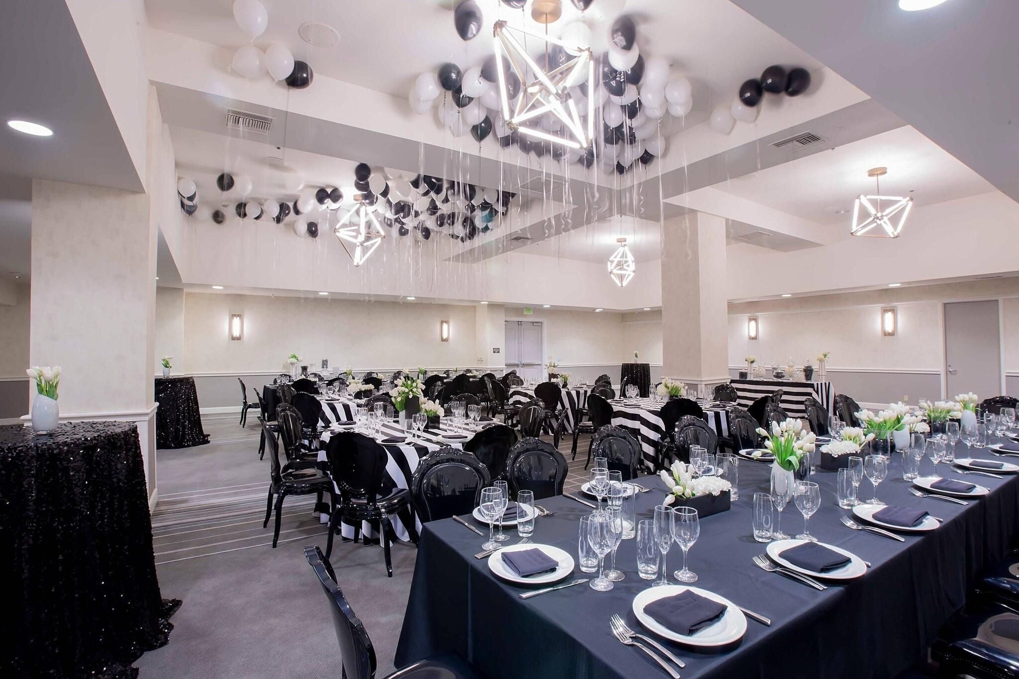 A banquet hall with tables set for dining, black and white chairs, and hanging decorations.