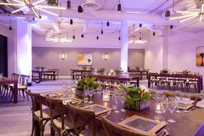 A spacious banquet hall with multiple dining tables, chairs, and modern lighting fixtures.