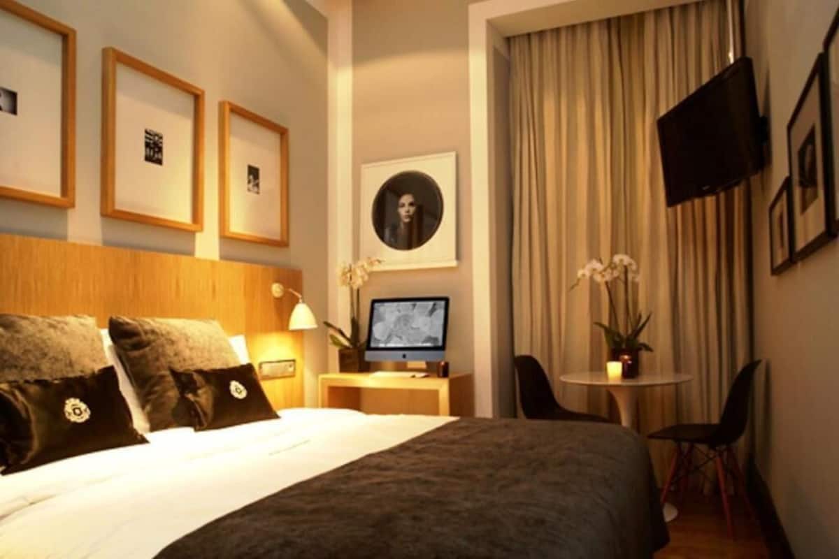 Ein Hotelzimmer mit Bett, Schreibtisch mit Computer, Fernseher und gerahmten Bildern an der Wand.