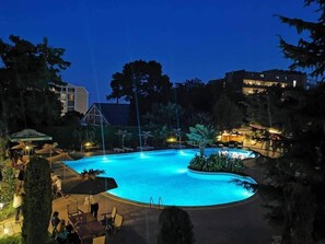 A swimming pool with lounge chairs and umbrellas, surrounded by trees and buildings. - Joya Park Complex (Varna)