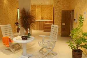 Una habitación con una mesa redonda, dos sillas blancas, una planta en maceta y una puerta de madera.