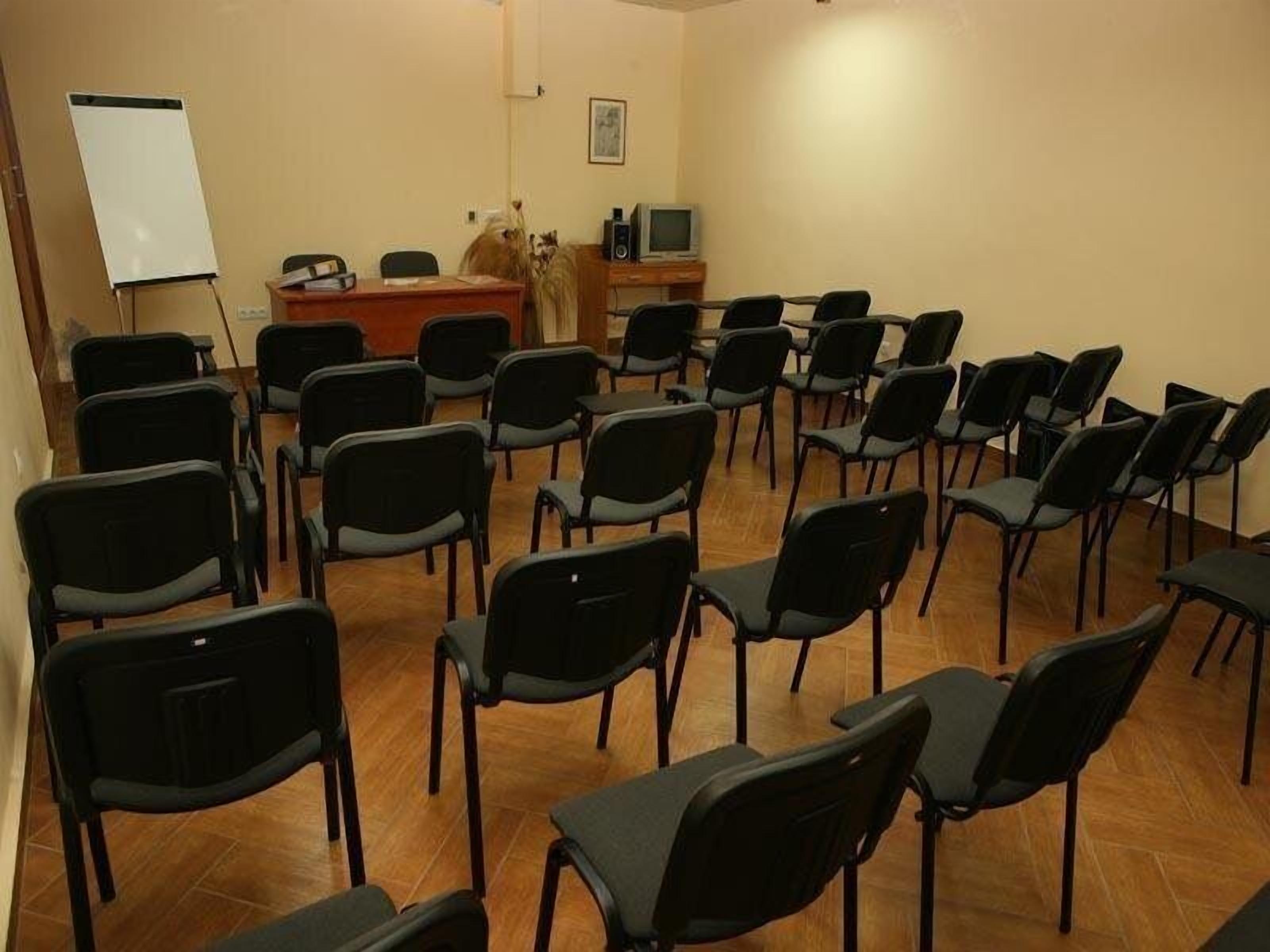 A conference room with rows of black chairs, a whiteboard, a desk with a computer, and a television.