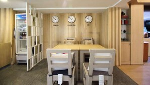 A dining area with a wooden wall, three clocks, and a refrigerator.