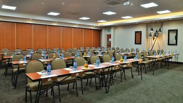 A conference room with rows of tables and chairs, water bottles, name tags, and a projector on the ceiling.