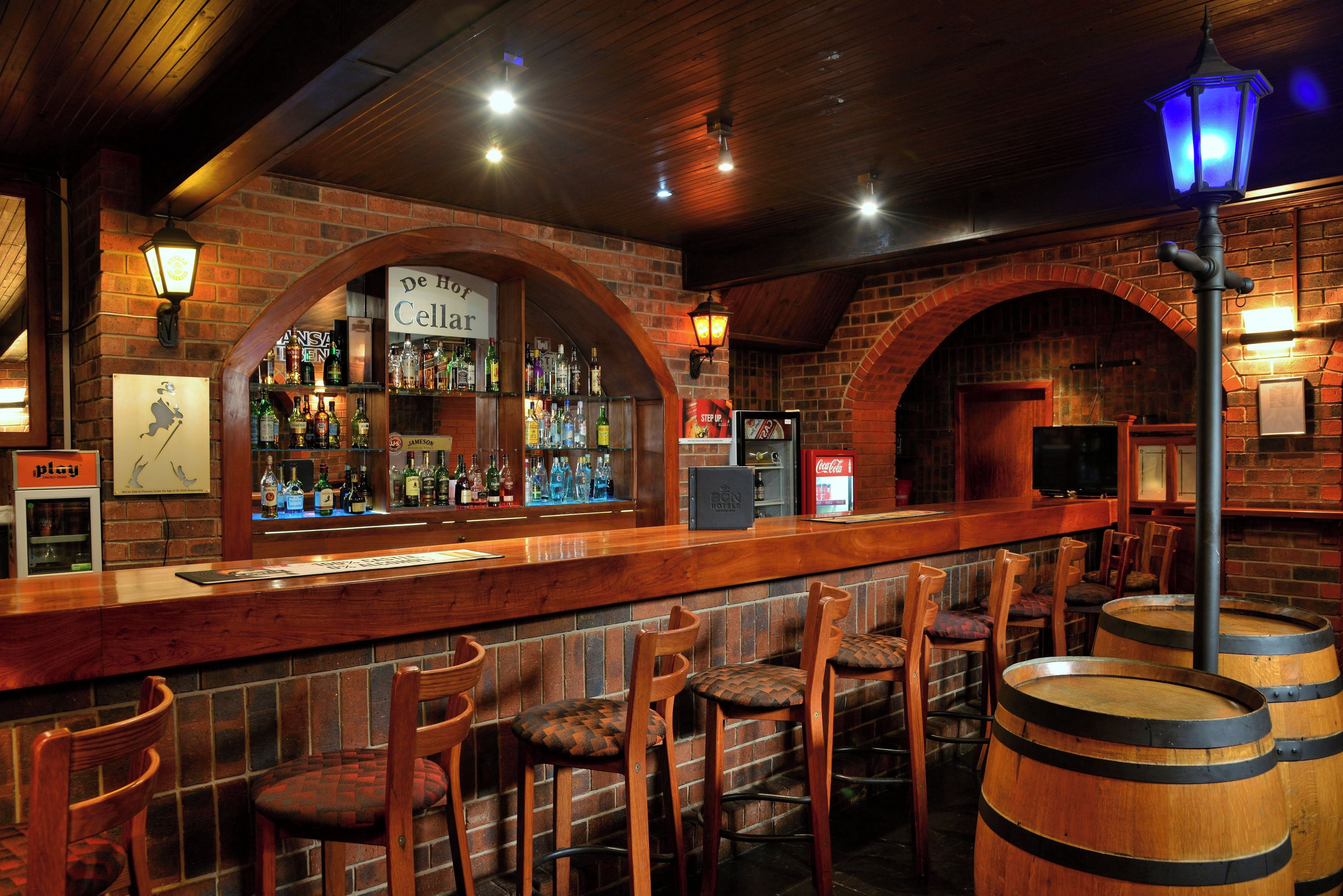 A bar area with wooden bar counters, stools, and a brick wall backdrop.