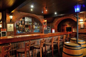A bar area with wooden bar counters, stools, and a brick wall backdrop. - Bon Hotel Empangeni (Empangeni)