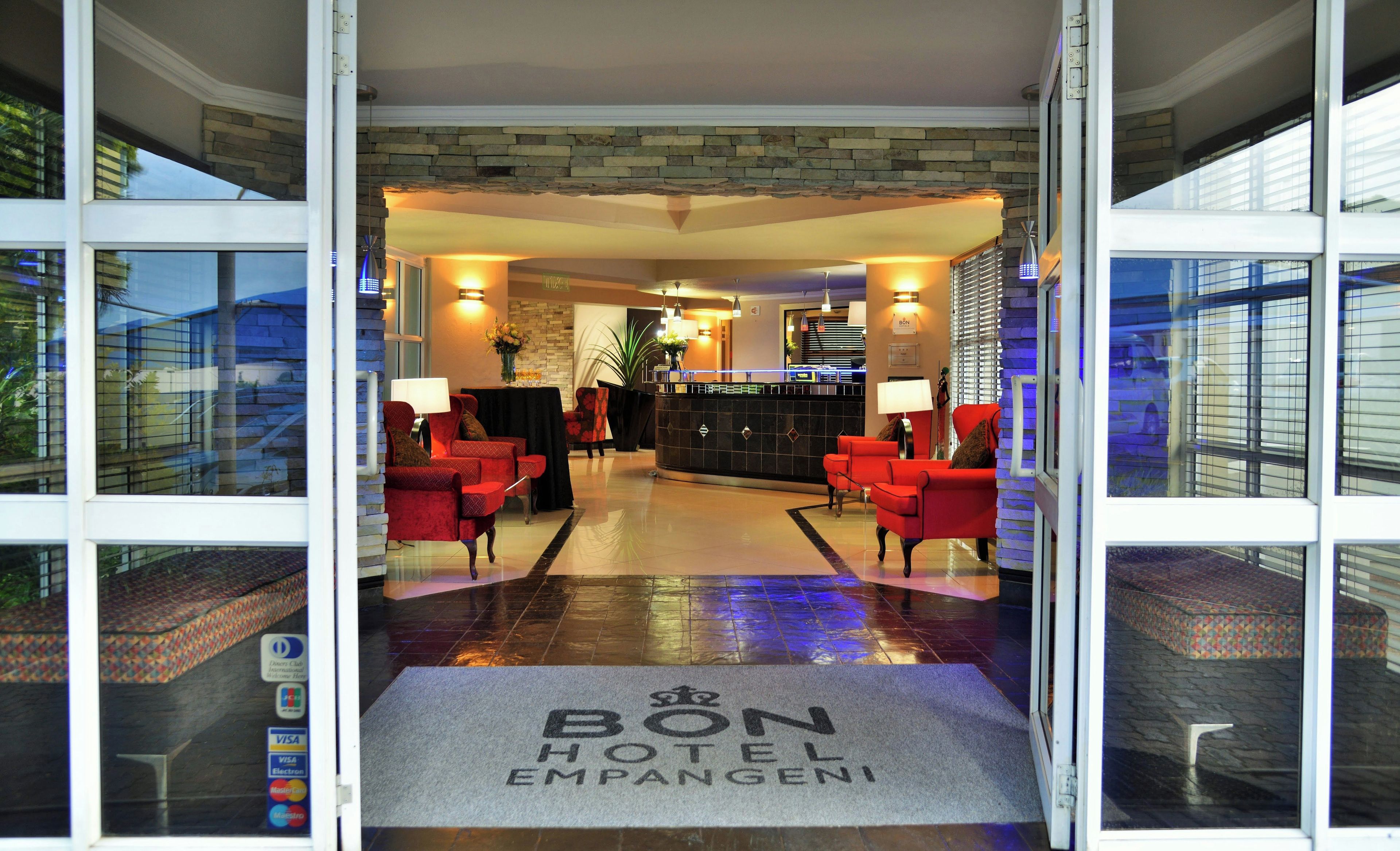 A hotel lobby with a reception desk, red seating area, and a doormat with the hotel's name.