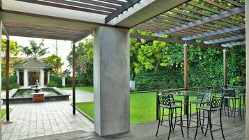 Ett takförsett utomhusområde med en pergola, sittplatser och en vattendekoration.