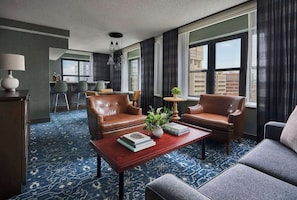 A hotel room with a sofa, armchairs, a coffee table, a lamp, and a view of the city through large windows. - Graduate by Hilton Minneapolis (Minneapolis)