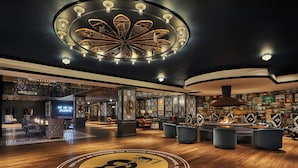 A spacious lobby with a central circular emblem, a high ceiling with a decorative light fixture, and a bar area with seating.
