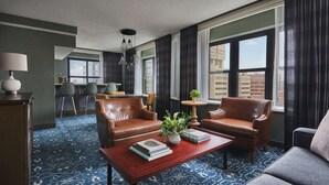A hotel room with a large window, a sofa, a coffee table, and a desk.
