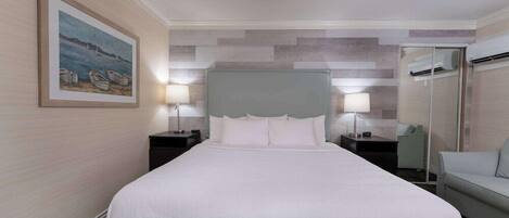 A hotel room with a large bed, two bedside tables with lamps, a grey headboard, a framed painting on the wall, and a grey sofa.