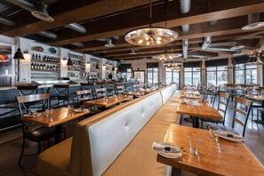 Un restaurant avec de longues tables en bois, des banquettes confortables et des lampes suspendues.