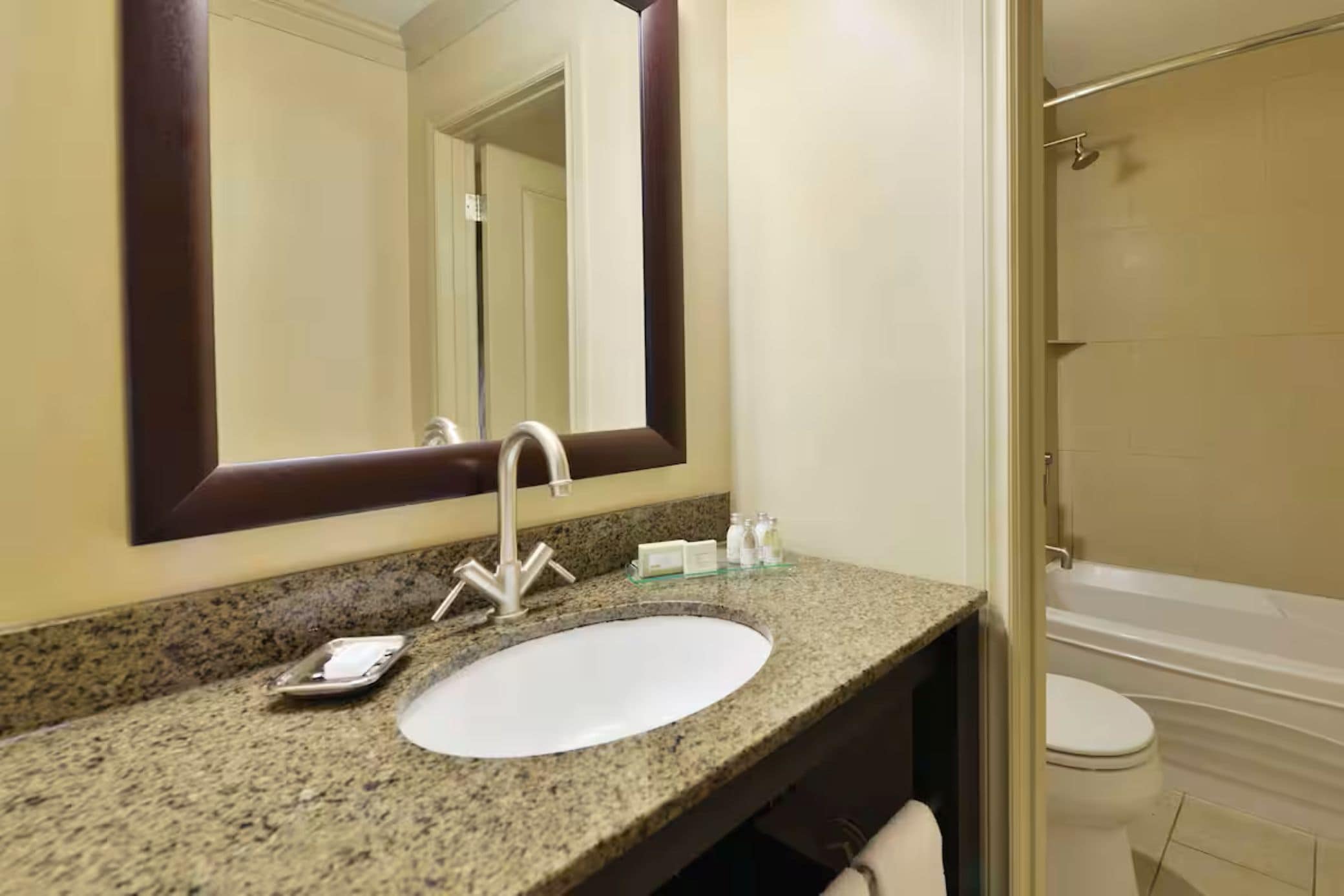 A bathroom with a granite countertop, a white sink, a large mirror, and a white bathtub.