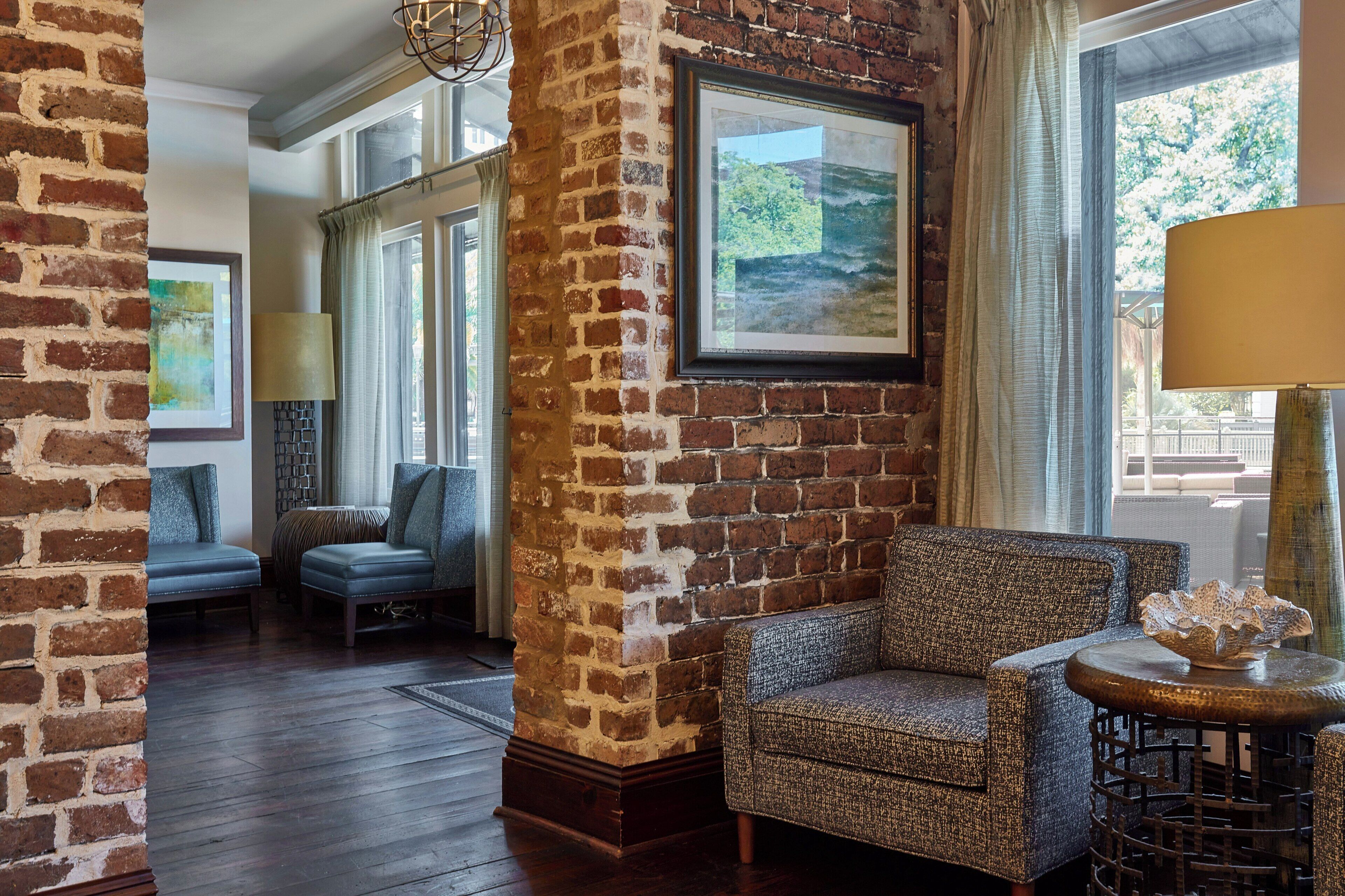 A room with a brick wall, a sofa, a chair, a lamp, and a window with a view.