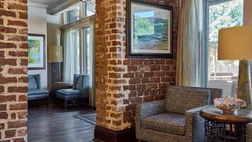 A room with a brick wall, a sofa, a chair, a lamp, and a window with a view.